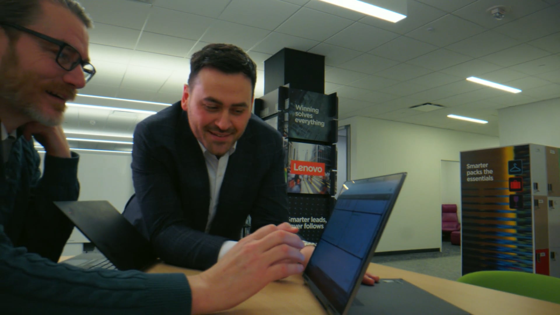 Two men in an office looking at a laptop screen together with smiling expressions.